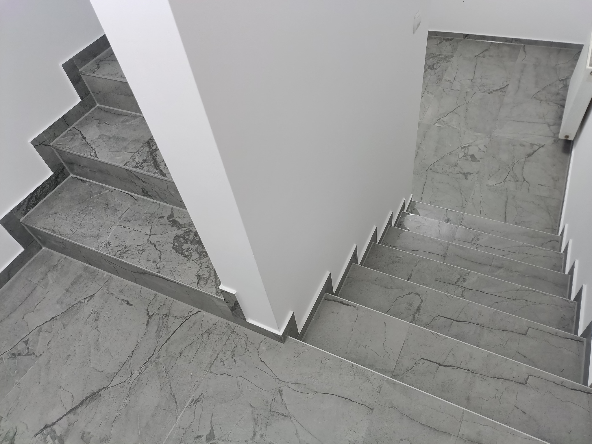 Widok z góry na wykończone schody z szarych płytek imitujących marmur, z białymi ścianami i listwami przypodłogowymi.