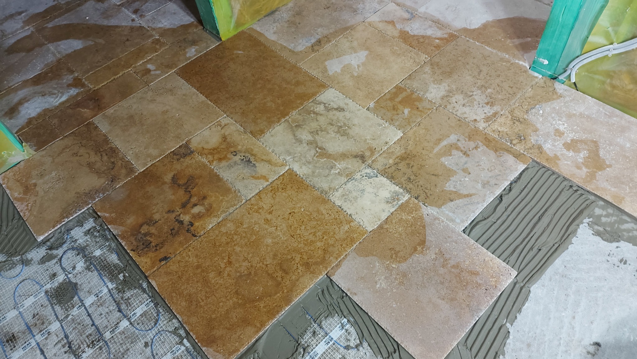 Układanie trawertynu na podłodze z ogrzewaniem podłogowym, widoczny klej z charakterystycznymi rowkami.