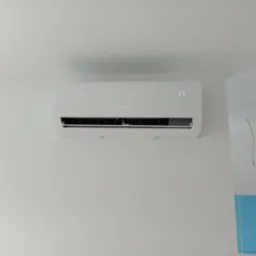 Biały klimatyzator MDV zamontowany na białej ścianie, wyświetlający temperaturę 17 stopni Celsjusza, z widocznym fragmentem niebieskiego zabezpieczenia na ścianie z prawej strony.