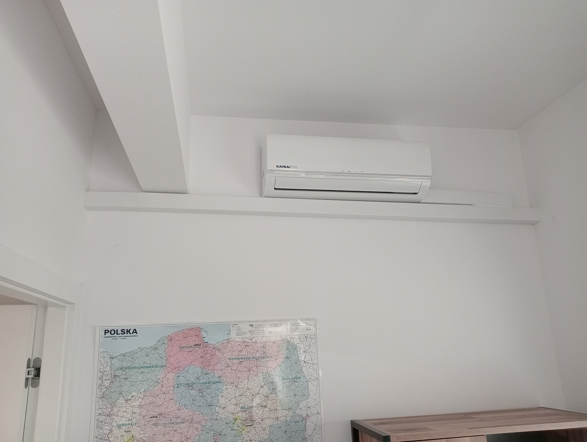 Wnętrze pokoju z zamontowaną jednostką wewnętrzną klimatyzacji Kaisai Eco na ścianie, pod sufitem, nad mapą Polski.