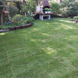 Anatolii Kononchuk Twój Ogrodnik - Świeżo ułożony trawnik z rolki w ogrodzie, z widocznym grillem ogrodowym, rabatami kwiatowymi i oczkiem wodnym w tle.