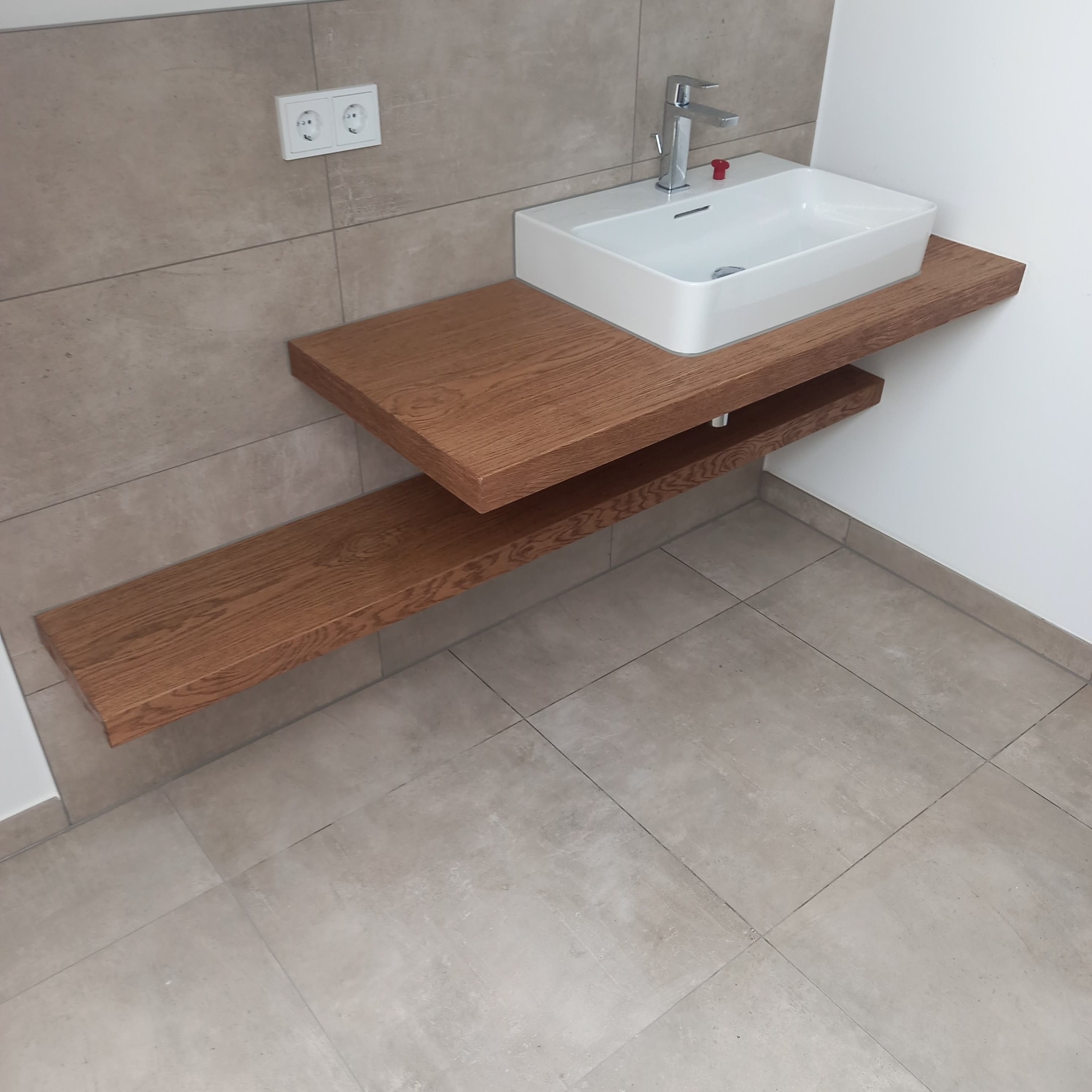 Nowoczesna łazienka z umywalką nablatową, chromowaną baterią i drewnianym blatem z półką, wykończona beżowymi płytkami.