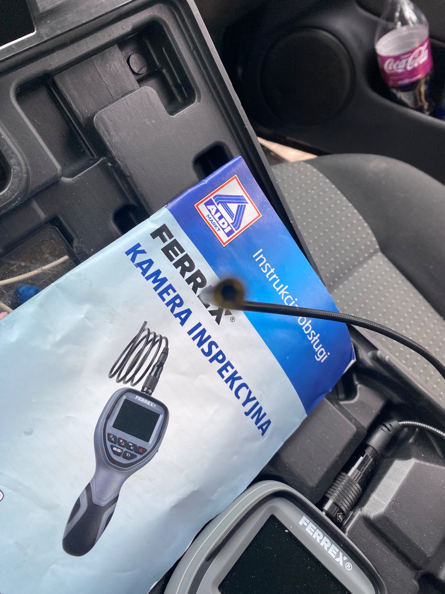 Kamera inspekcyjna Ferrex z instrukcją obsługi, leżąca w schowku samochodowym, widoczna końcówka kamery na giętkim przewodzie.