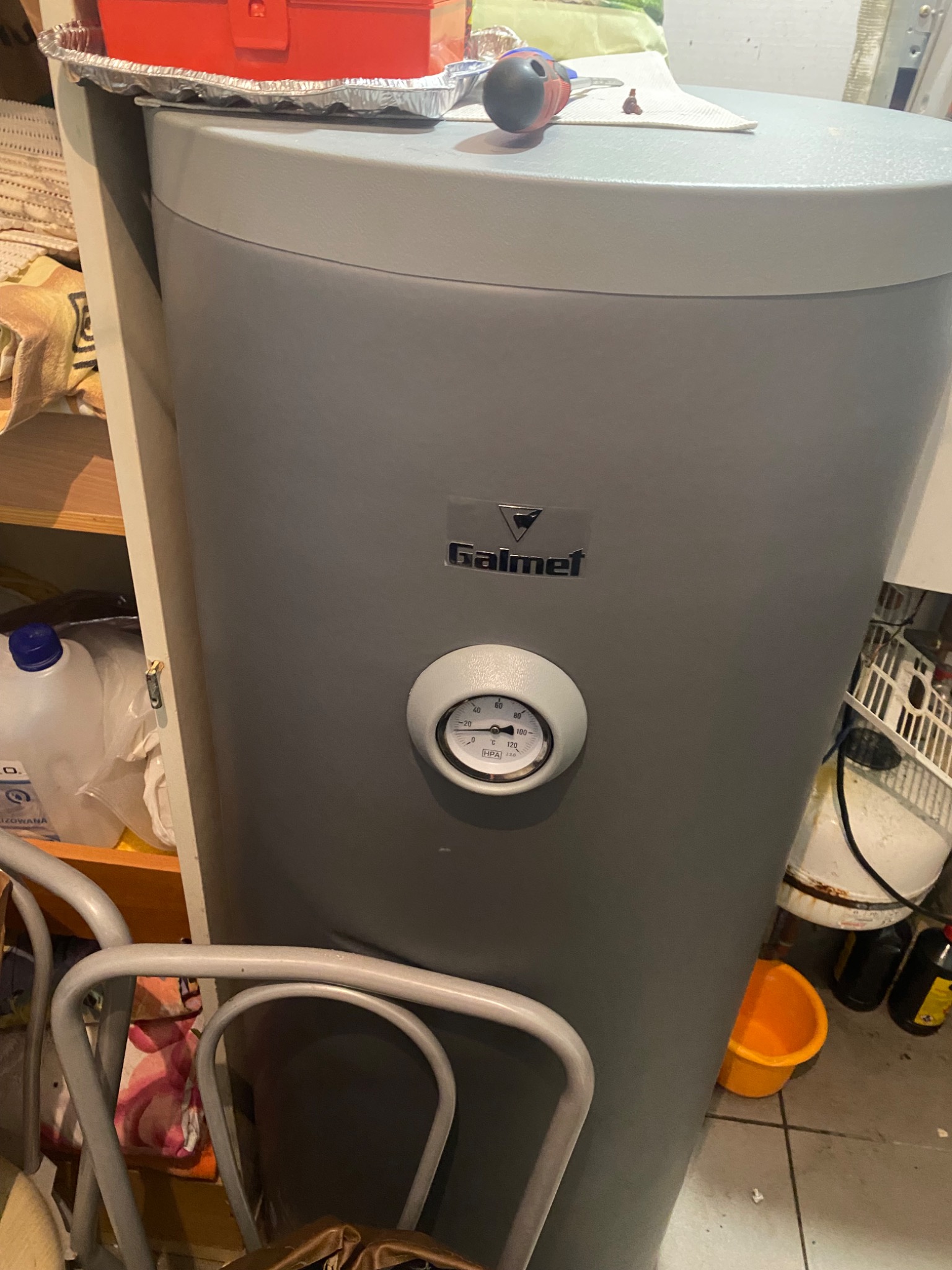 Szary bojler Galmet z widocznym manometrem wskazującym ciśnienie, narzędzia i skrzynka narzędziowa na górze, otoczenie robocze.