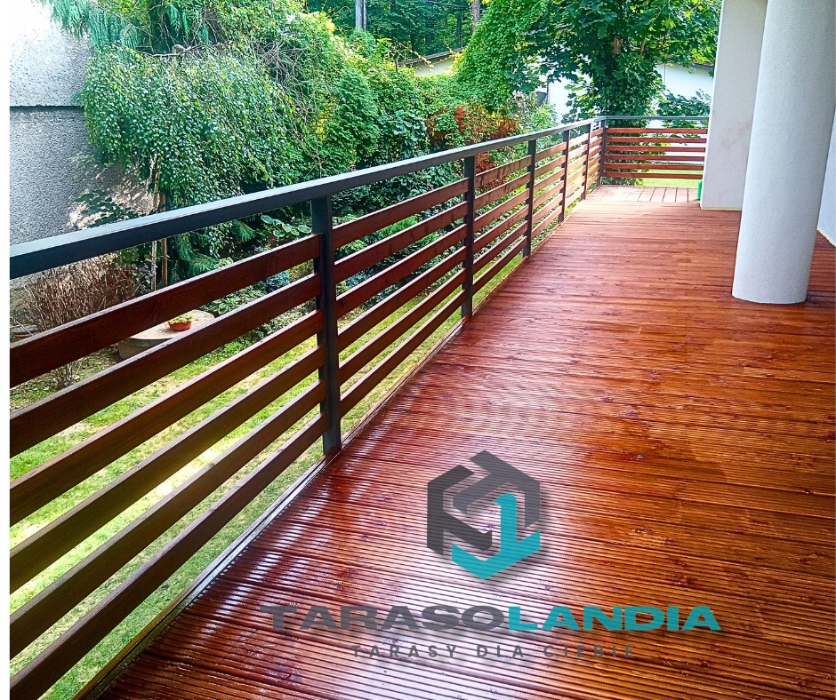 Błyszczący, świeżo zaimpregnowany taras z drewna egzotycznego z ciemnymi, poziomymi balustradami i metalową poręczą, widok na zieleń ogrodu.