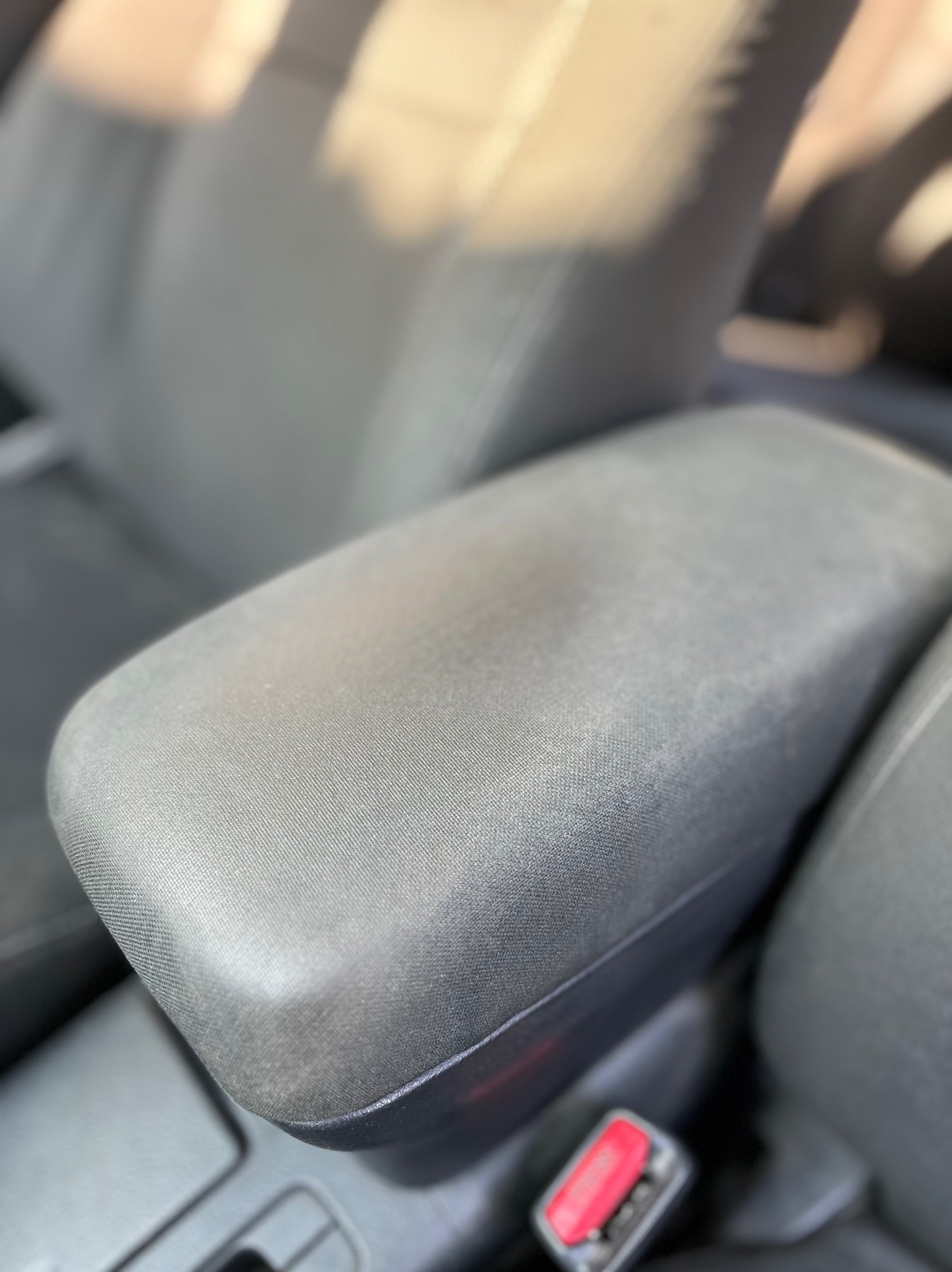 Szczegółowe ujęcie tapicerowanego podłokietnika samochodowego we wnętrzu auta w Wierzchucicach, widoczny fragment czerwonego zapięcia pasa bezpieczeństwa.