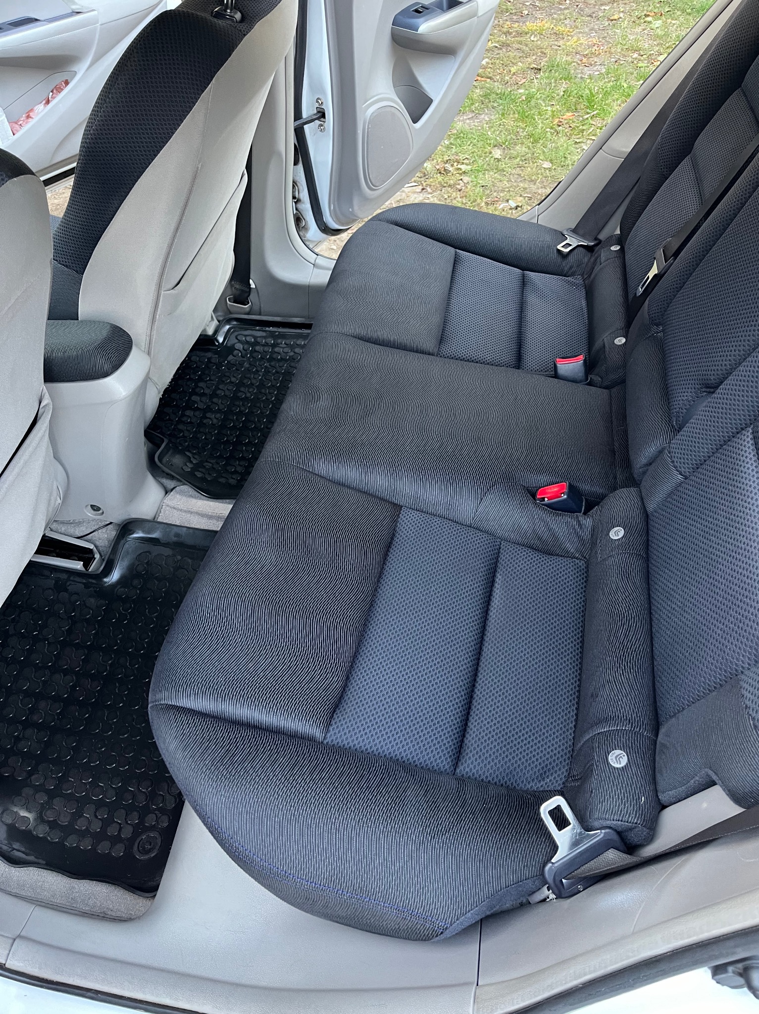 Wnętrze samochodu z czarną tapicerką na tylnych siedzeniach, widoczne pasy bezpieczeństwa i gumowe dywaniki.