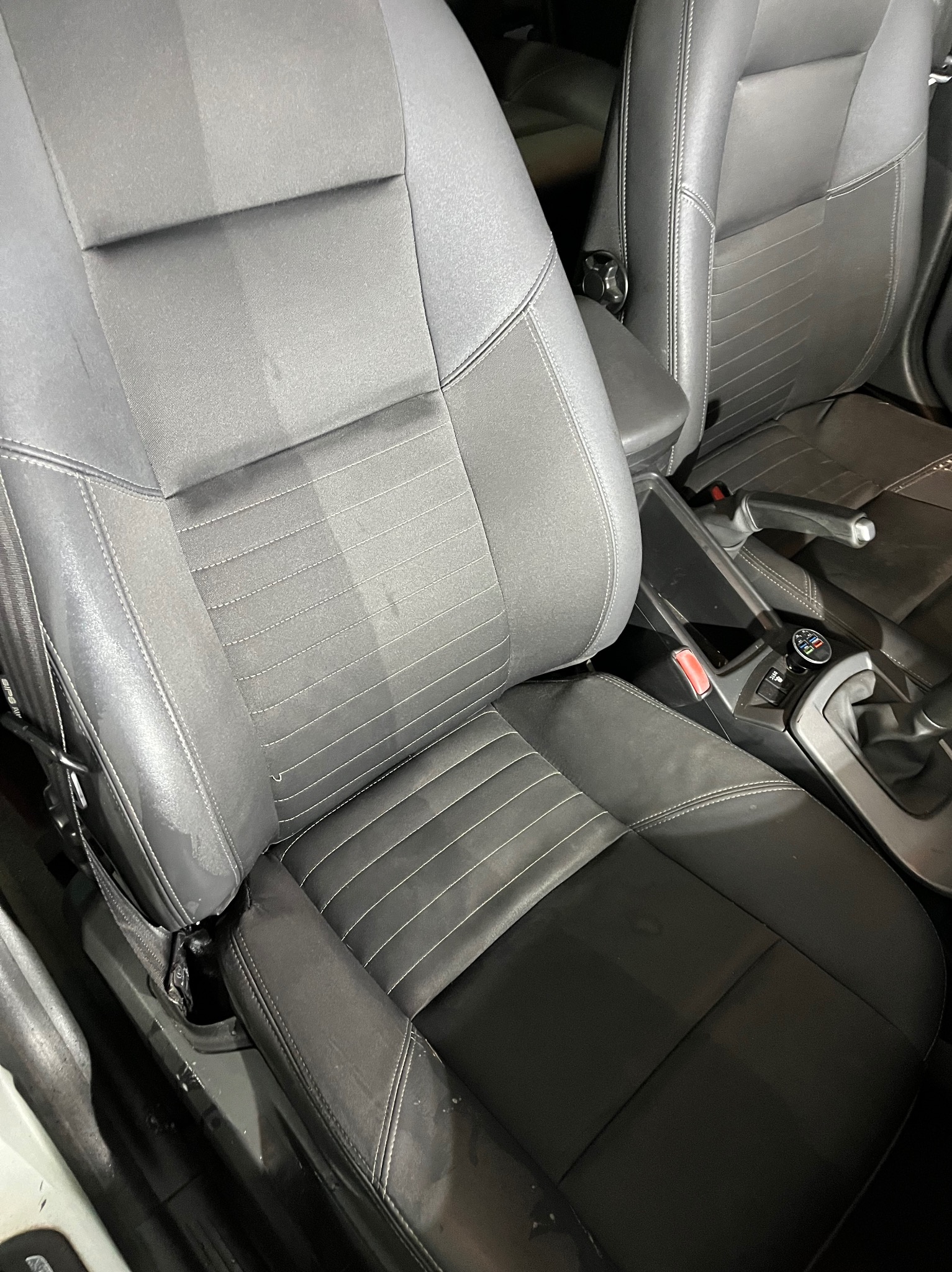 Szary fotel samochodowy z widoczną różnicą w czystości po lewej stronie, jasna smuga po czyszczeniu na tle ciemniejszej, zabrudzonej reszty fotela.