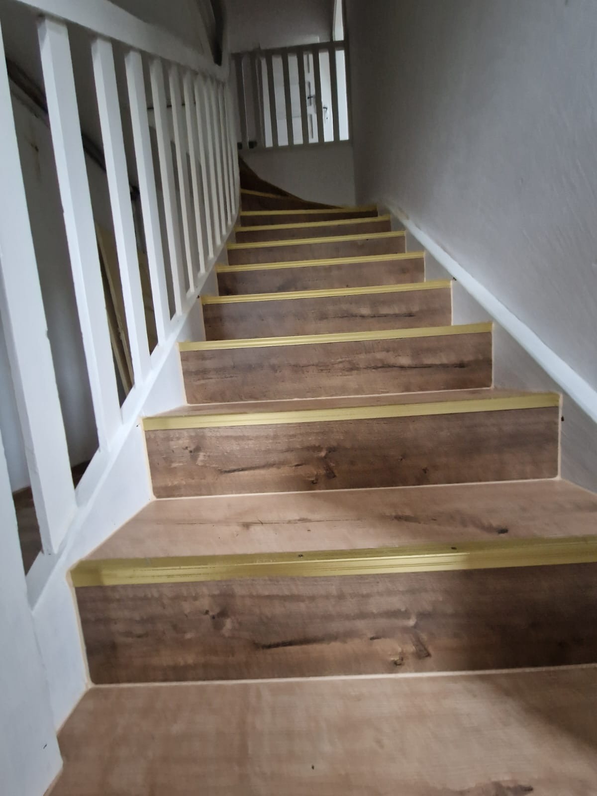 Schody wewnętrzne wykończone panelami imitującymi drewno, zabezpieczone złotymi listwami krawędziowymi, biała balustrada