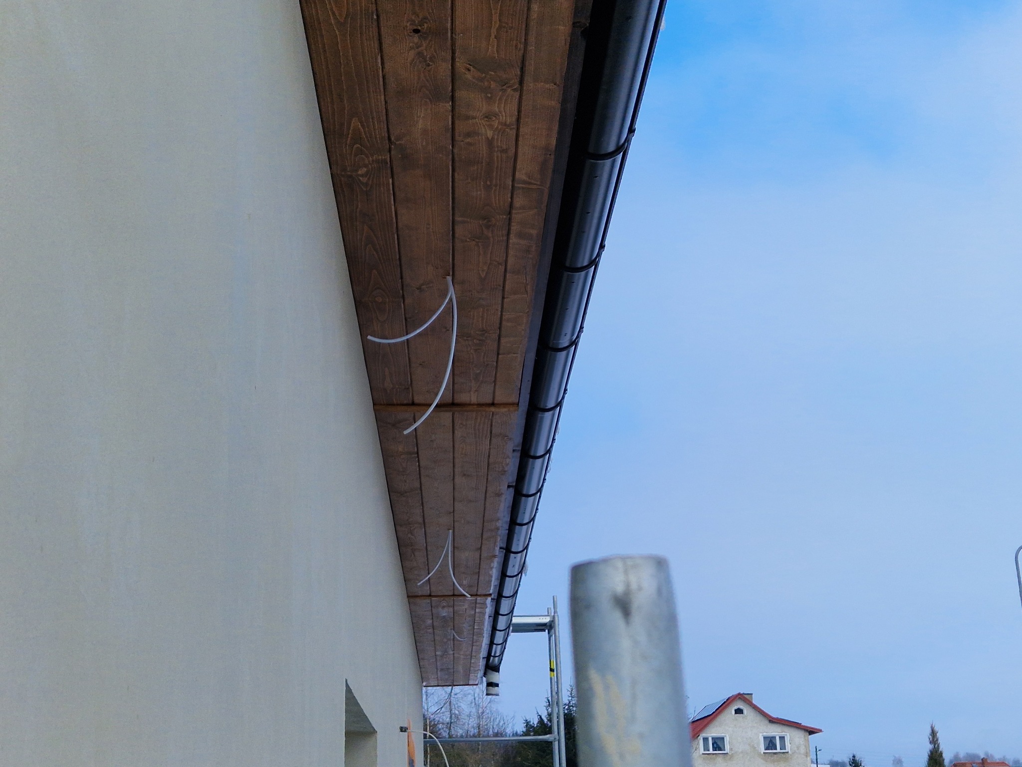 Drewniana podbitka dachowa z zamontowaną rynną, widok z dołu na elewację budynku i fragment rusztowania.