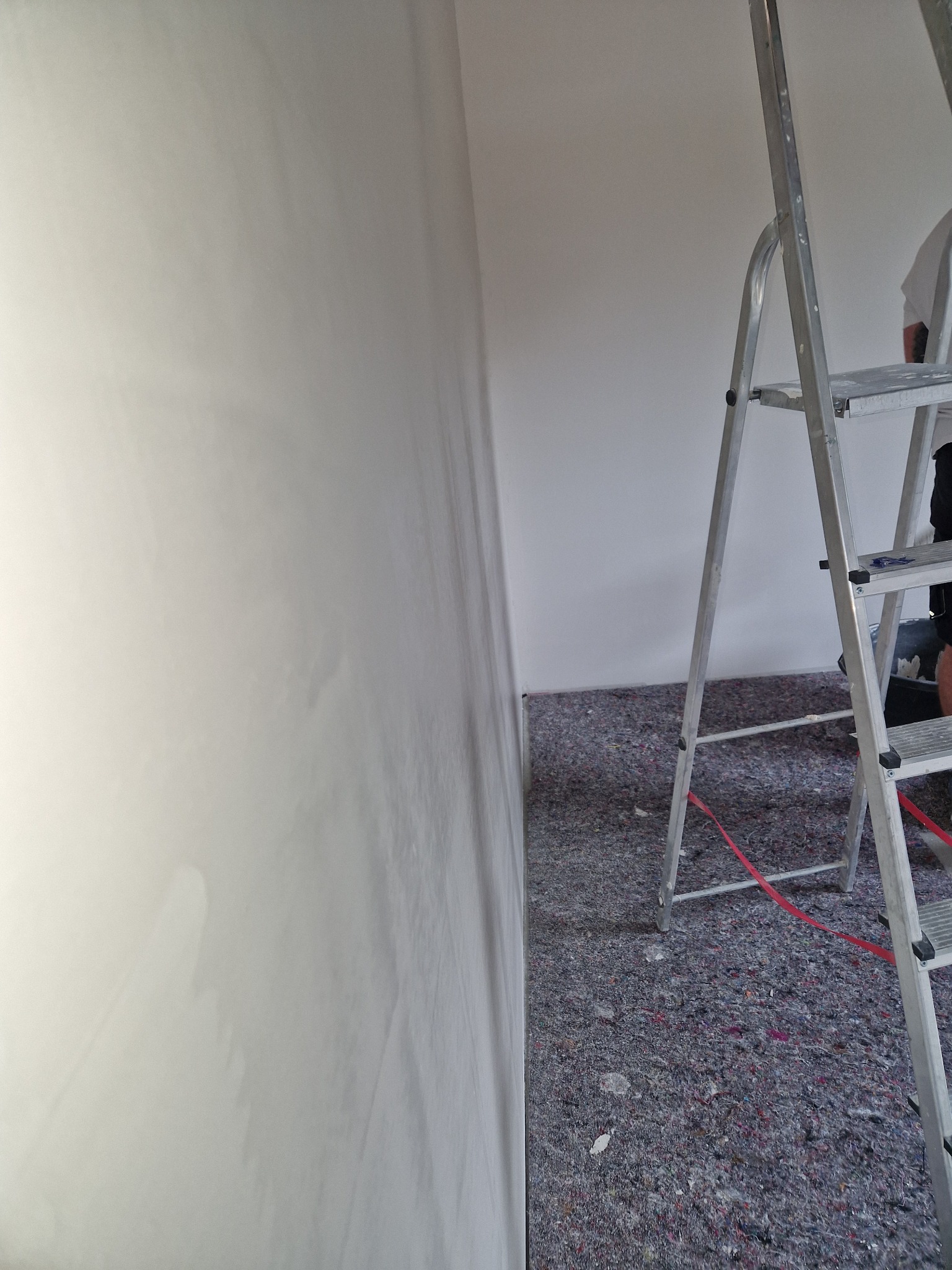 Świeżo nałożona gładź na ścianie, widoczna aluminiowa drabina i zabezpieczona podłoga przed dalszymi pracami wykończeniowymi.