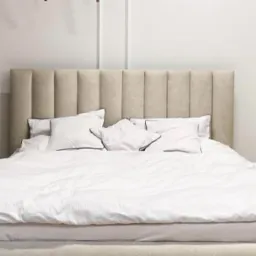Beżowy tapicerowany zagłówek łóżka z pionowymi przeszyciami, biała pościel i poduszki z czarną lamówką w minimalistycznej sypialni.