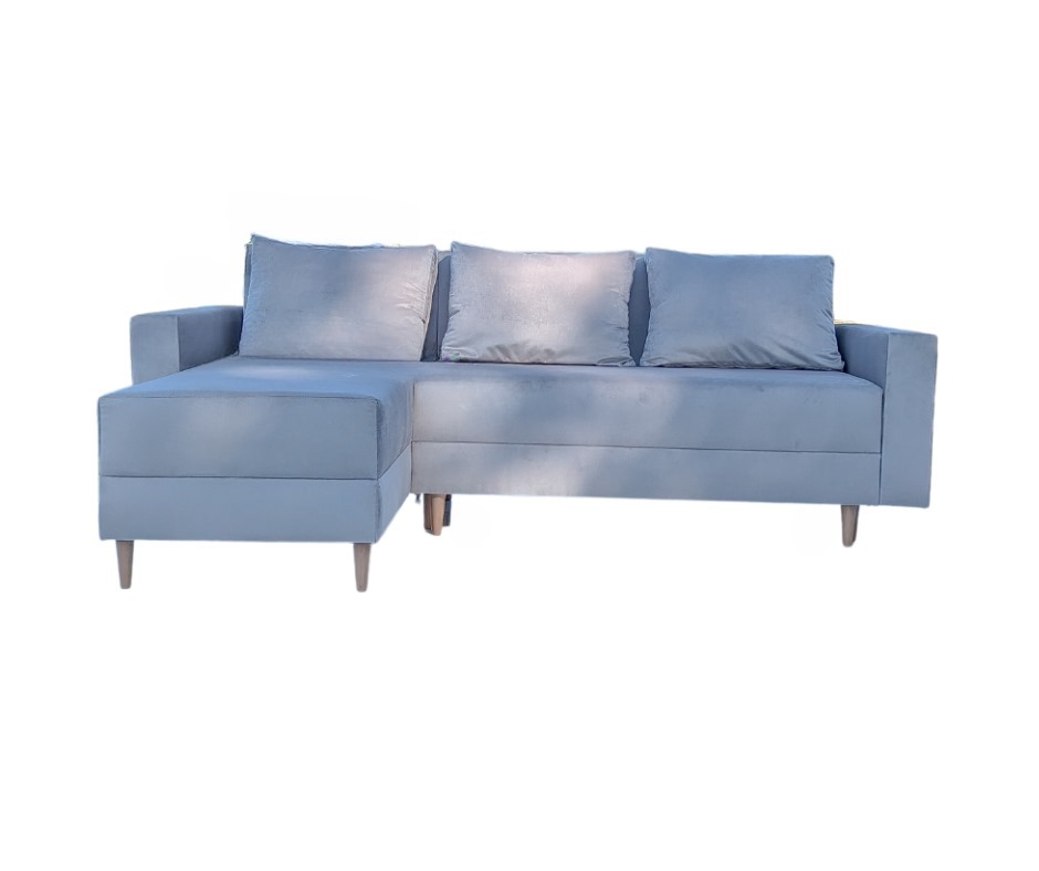 Narożnik z jasnoniebieską, pluszową tapicerką i trzema poduszkami, ustawiony na drewnianych nóżkach.