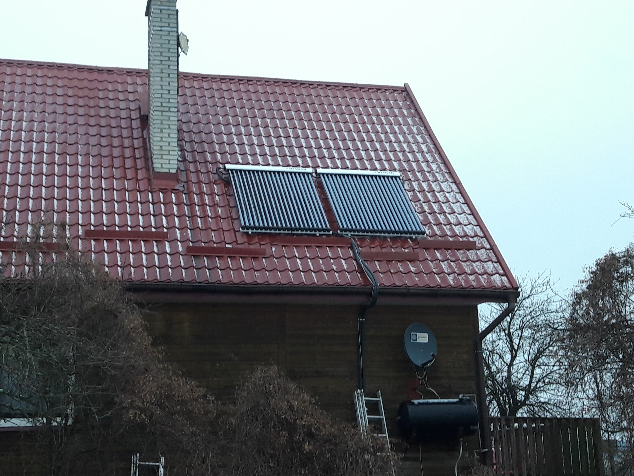 Dwa kolektory słoneczne na czerwonym dachu domu w Juchnowcu Kościelnym, widok z dołu, pochmurne niebo.