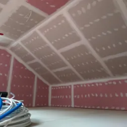 Poddasze w trakcie zabudowy płytami gipsowo-kartonowymi, widoczne łączenia szpachlowane, instalacja elektryczna w peszlu na podłodze, surowe wykończenie.