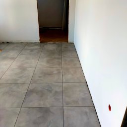 AB4 Artur Bukała - Szare płytki podłogowe ułożone w nowym pomieszczeniu z białymi ścianami, widoczny fragment czerwonego znacznika na ścianie.