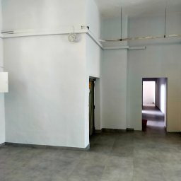 AB4 Artur Bukała - Wnętrze biura po malowaniu ścian na biało, szara podłoga z płytek, widoczne kable pod sufitem.