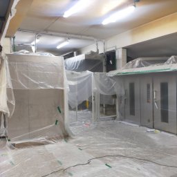 AB4 Artur Bukała - Przygotowanie do prac w pomieszczeniu przemysłowym, zabezpieczone folią malarską ściany, podłoga i urządzenia, widoczne zielone taśmy mocujące.