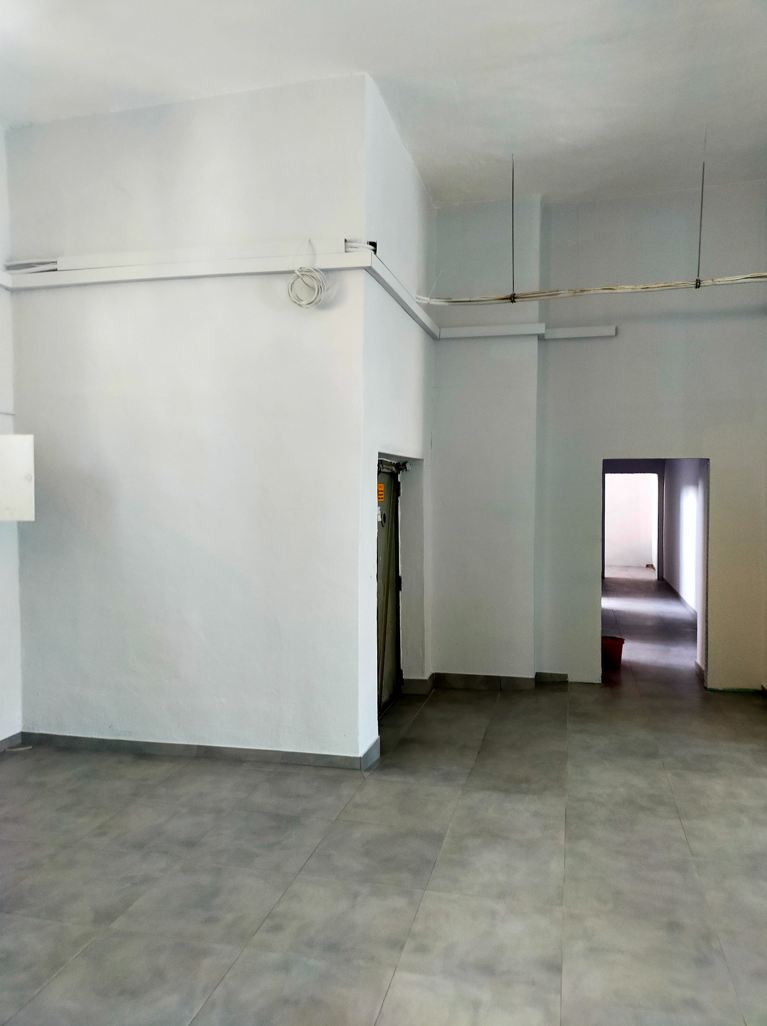 Wnętrze biura po malowaniu ścian na biało, szara podłoga z płytek, widoczne kable pod sufitem.