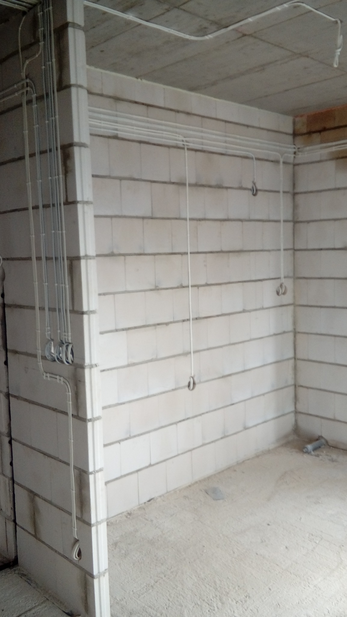 Surowy pokój z białych bloczków z widocznymi przewodami elektrycznymi zamontowanymi na ścianach i suficie, brak wykończenia.