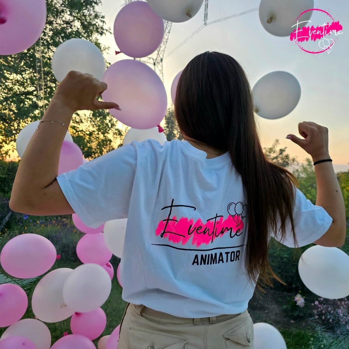Osoba w koszulce z napisem 'Eventime Animator' na tle różowych i białych balonów, pozująca z podniesionymi rękami.
