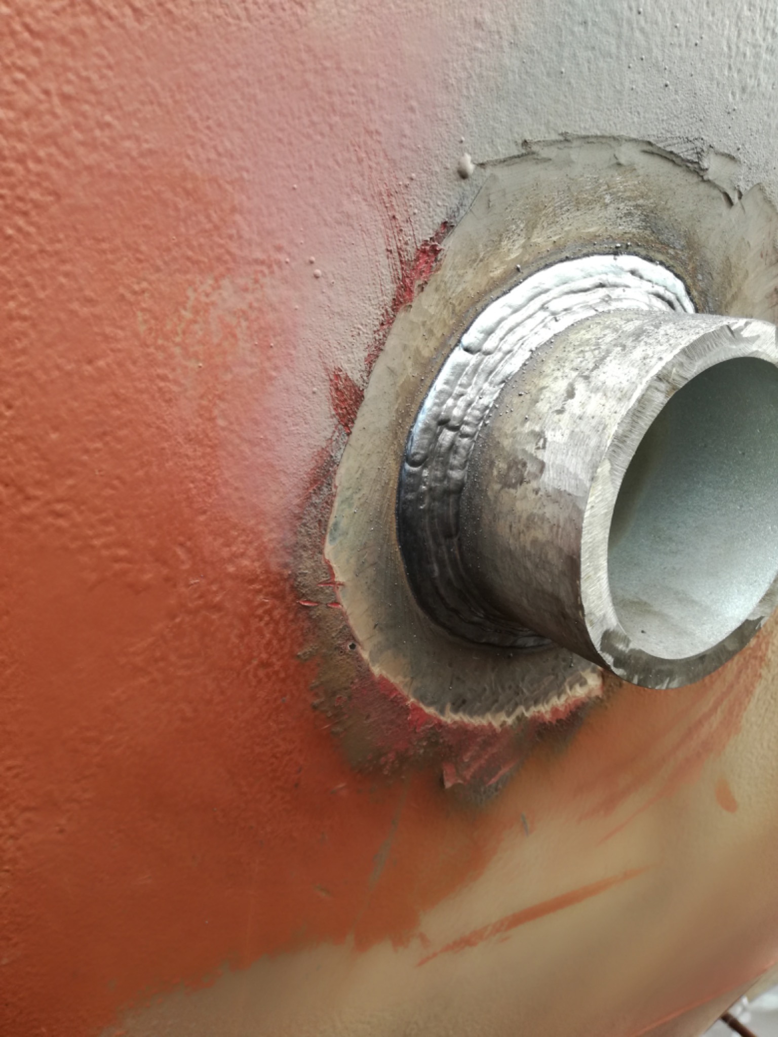 Spoina łącząca rurę ze zbiornikiem, widoczne ślady po spawaniu i przygotowaniu powierzchni, pomarańczowa farba na zbiorniku, szlifowana krawędź rury.