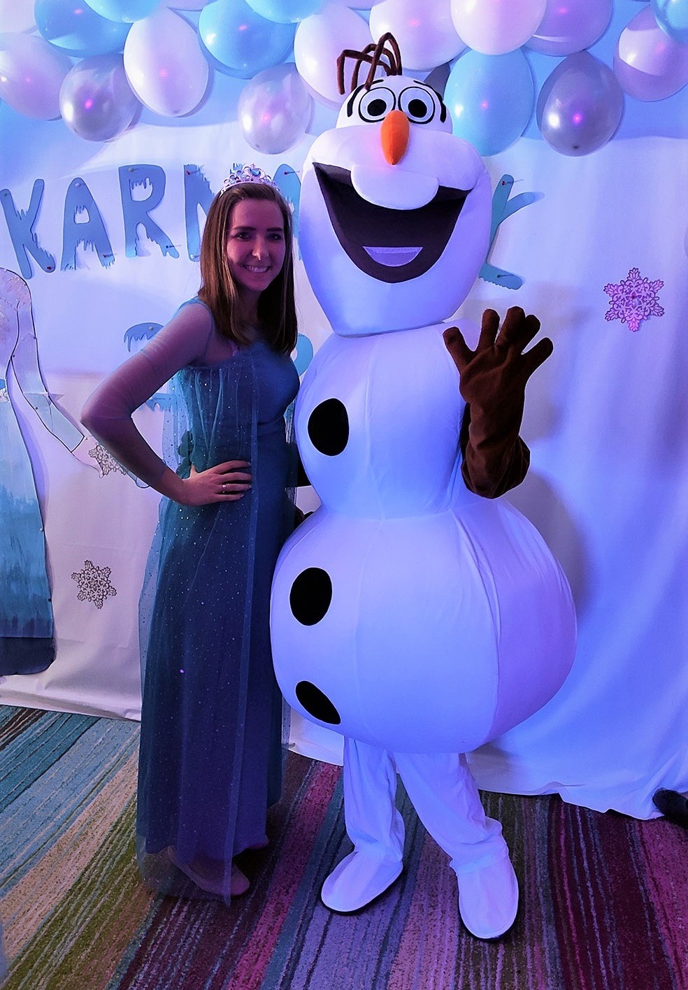 Kobieta w kostiumie Elsy z Krainy Lodu pozuje obok dmuchanego Olafa na tle dekoracji balonowych i napisu 'KARNAWAŁ'.