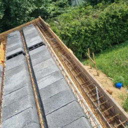 Wznoszenie ścian z bloczków betonowych zbrojonych stalą, widok z góry na budowę w otoczeniu zieleni.