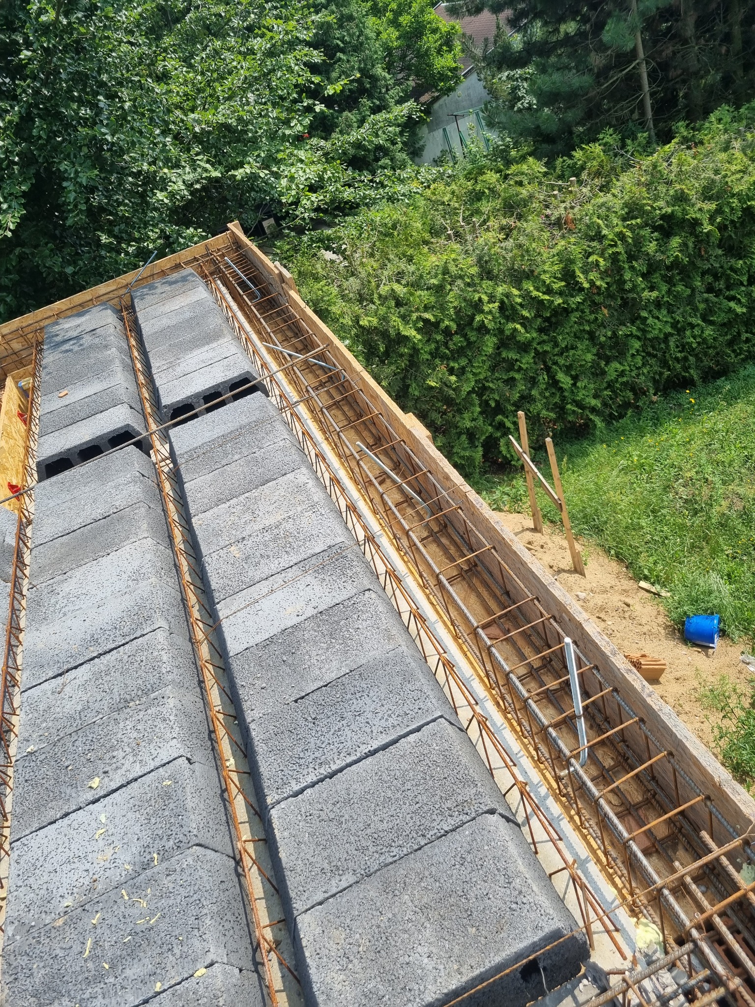 Wznoszenie ścian z bloczków betonowych zbrojonych stalą, widok z góry na budowę w otoczeniu zieleni.