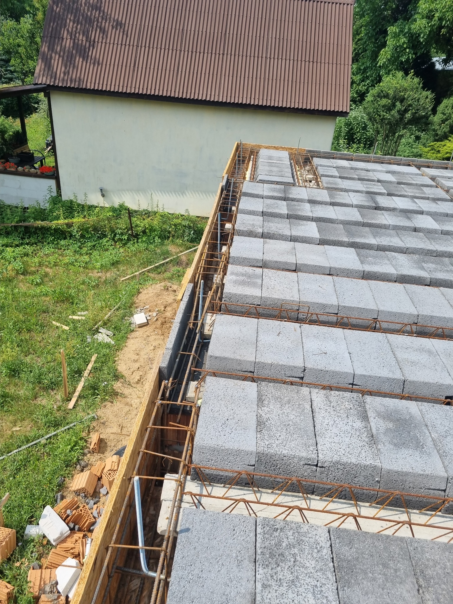 Wznoszenie stropu Teriva z szarych bloczków betonowych, zbrojenie stalowe ułożone między bloczkami, widoczne drewniane szalunki i fragment budynku w tle.