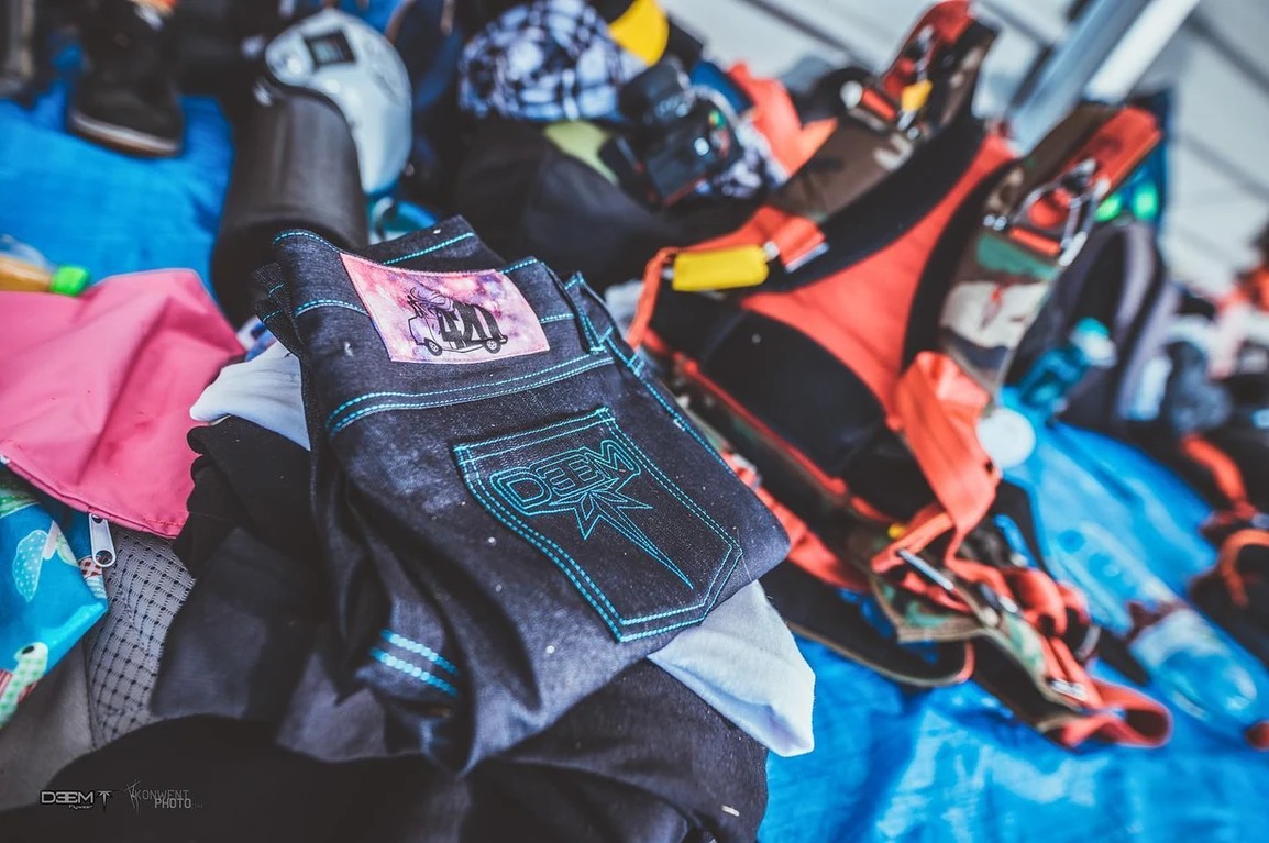 Stos ubrań z dżinsami z unikalnym wzorem kieszeni i naszywką, leżący na niebieskim tle w warszawskim zakładzie.