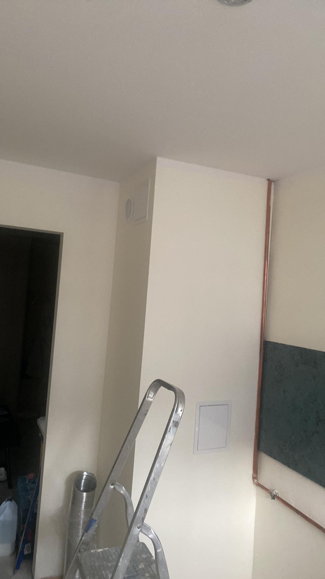 Wnętrze w trakcie prac: ściana pomalowana na biało, widoczne rury miedziane, otwór wentylacyjny, drabina aluminiowa i rura wentylacyjna.