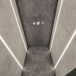 Vasyl Smachynskyi - Wąskie wnętrze wykończone mozaiką w odcieniach szarości i oświetleniem LED, widok z dołu na sufit z trzema punktowymi lampami.