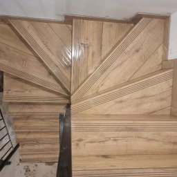 Vasyl Smachynskyi - Klatka schodowa wykończona płytkami imitującymi drewno, z widocznymi detalami wzoru i faktury płytek oraz metalową barierką po lewej stronie