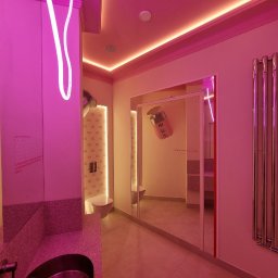 Vasyl Smachynskyi - Nowoczesna łazienka w różowym oświetleniu neonowym. Lustrzane drzwi, dekoracyjna ściana z motywem 'R', designerska umywalka, grzejnik drabinkowy.