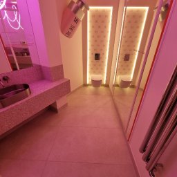 Vasyl Smachynskyi - Nowoczesna toaleta z umywalką na blacie z lastryko, lustrami i neonowym oświetleniem w odcieniach różu. Widoczne detale wykończeniowe i armatura.