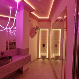 Vasyl Smachynskyi - Różowa łazienka z neonami i designerską umywalką. Na ścianie dekoracja w kształcie butelki perfum. W tle toalety z podświetleniem i lustro.