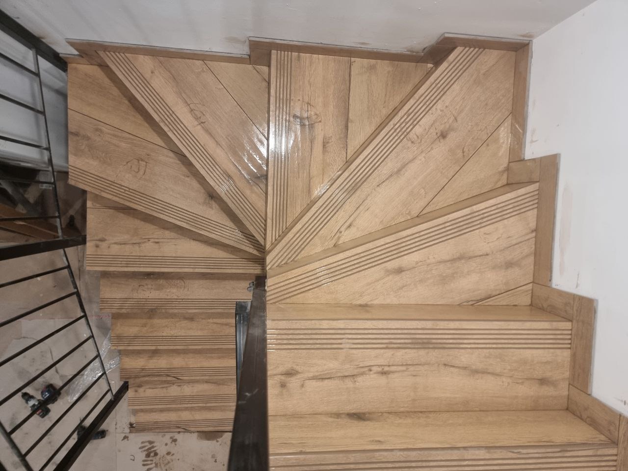 Klatka schodowa wykończona płytkami imitującymi drewno, z widocznymi detalami wzoru i faktury płytek oraz metalową barierką po lewej stronie