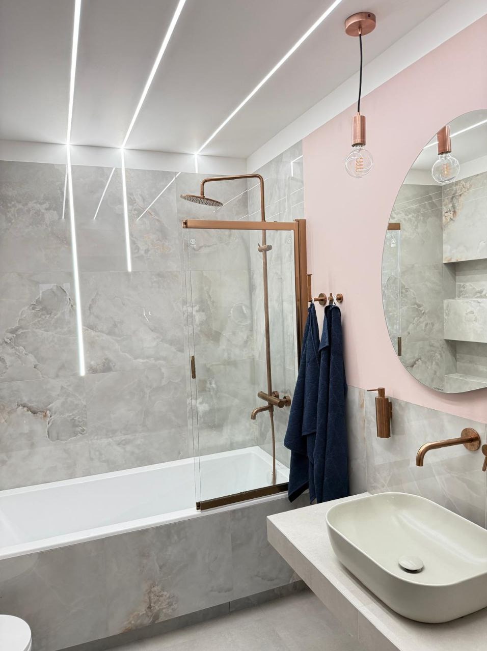 Nowoczesna łazienka z wanną, szklanym parawanem, okrągłym lustrem i oświetleniem LED w suficie. Armatura w kolorze miedzi.