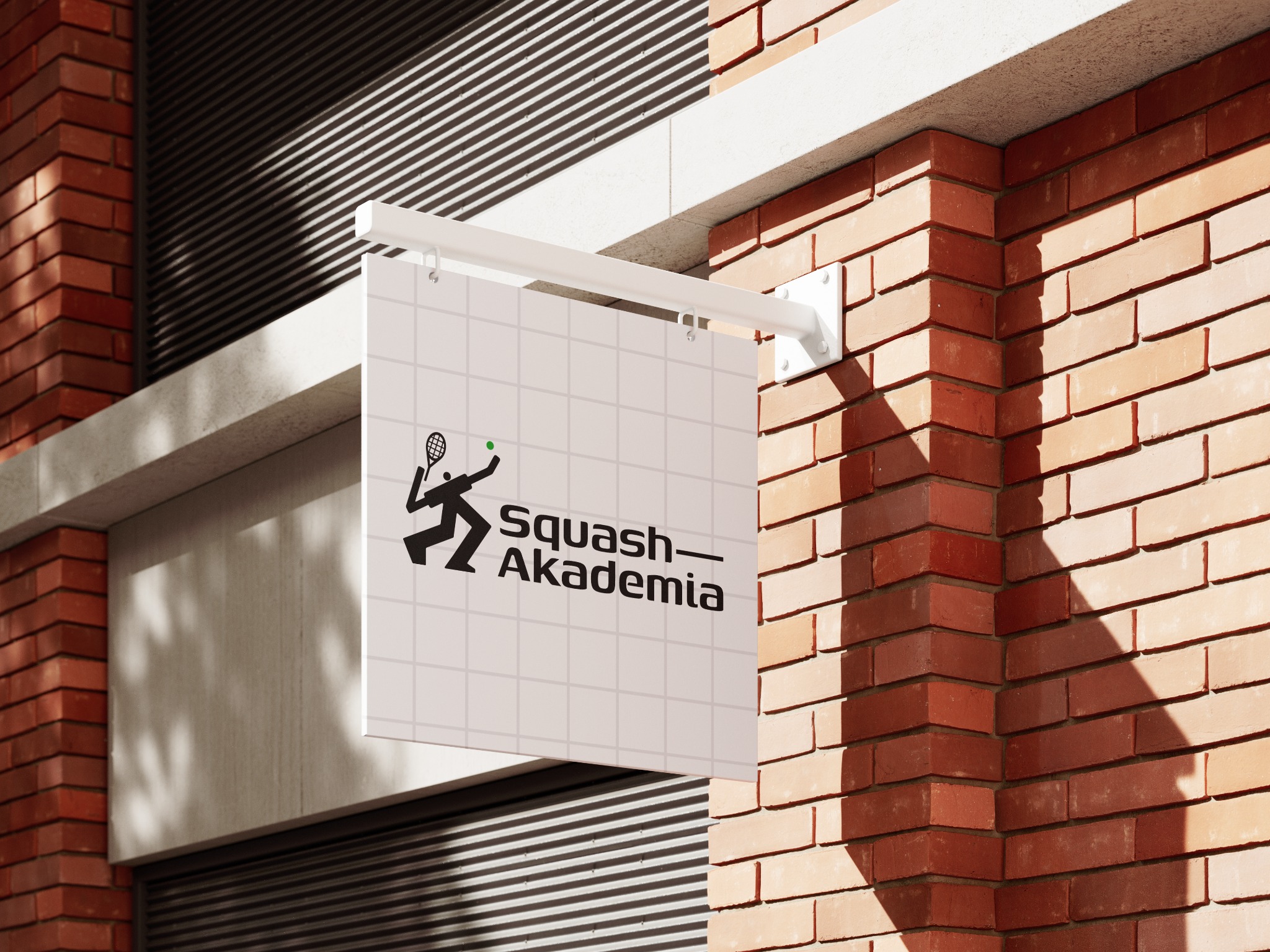 Zewnętrzny szyld z logotypem Squash Akademia, umieszczony na ceglanej ścianie budynku.