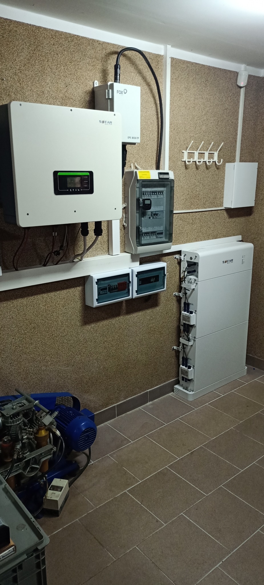 Kompletna instalacja fotowoltaiczna w pomieszczeniu: inwerter SOFAR z wyświetlaczem, moduł FOX, rozdzielnica elektryczna, dwa liczniki energii i bateria SOFAR, a na podłodze kompresor.