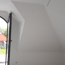 Usługi Remontowe i Wykończeniowe - Poddasze z oknem dachowym, świeżo pomalowane na biało, widoczne ślady po malowaniu na podłodze, wystający kabel ze ściany.
