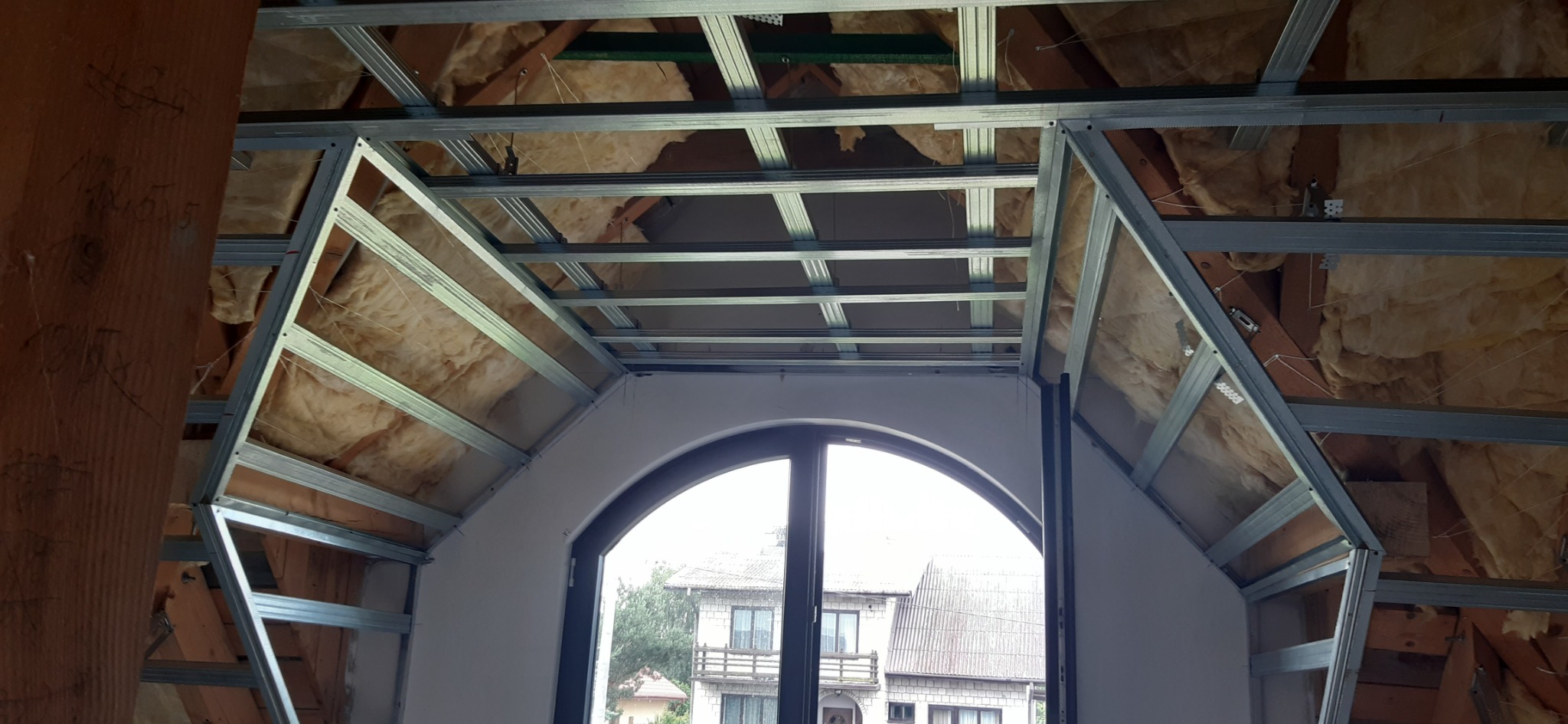 Montaż metalowej konstrukcji sufitu podwieszanego z izolacją wełną mineralną w poddaszu z oknem łukowym.