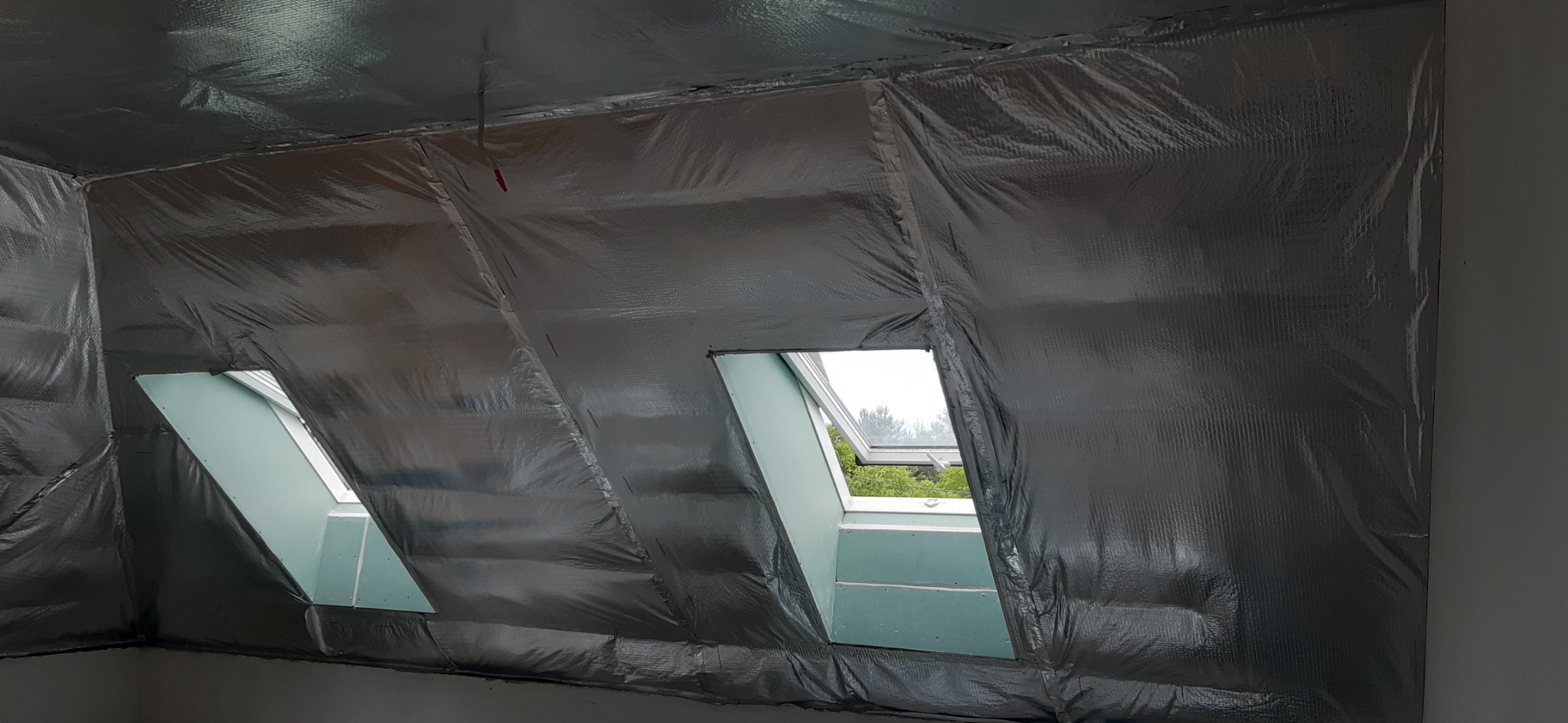 Poddasze z oknami dachowymi w trakcie izolacji folią aluminiową, widoczne łączenia folii i fragment ściany.