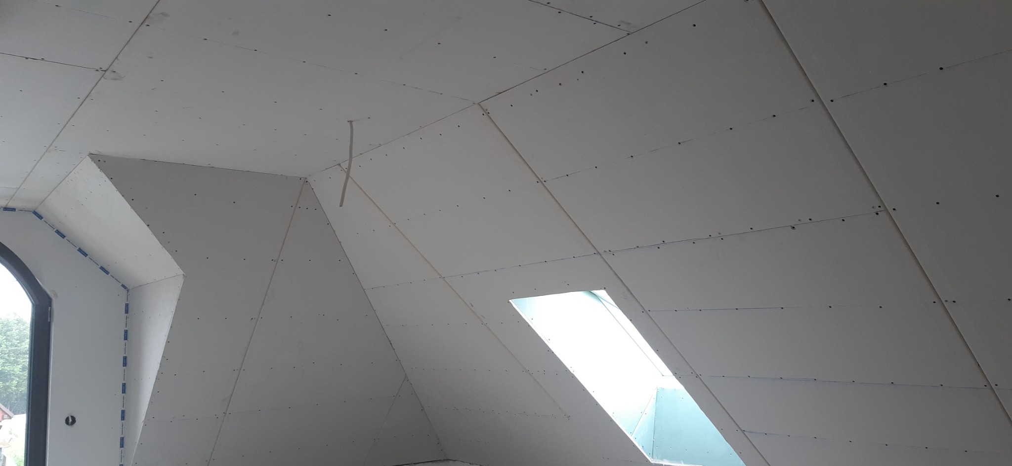 Poddasze z oknami dachowymi w trakcie montażu płyt kartonowo-gipsowych, widoczne łączenia płyt i otwór na okno.