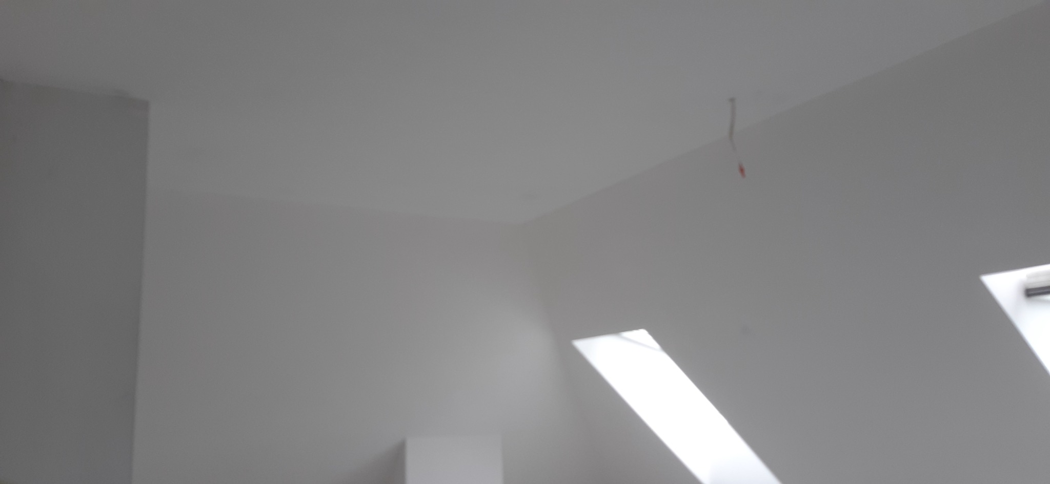 Białe, świeżo pomalowane poddasze w Radomiu z oknami dachowymi i wystającym kablem ze ściany.