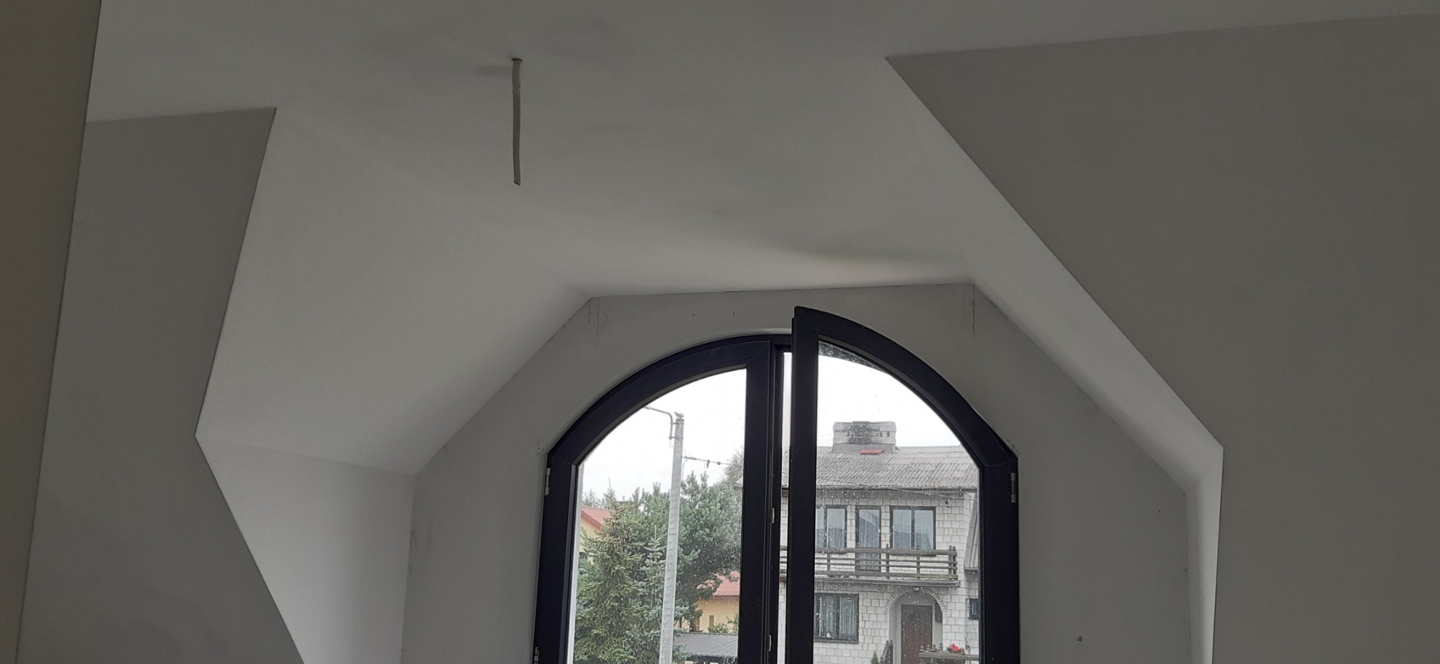 Poddasze po malowaniu na biało z charakterystycznym oknem łukowym w czarnej ramie, widoczny kabel wystający z sufitu, ślady po malowaniu na oknie.