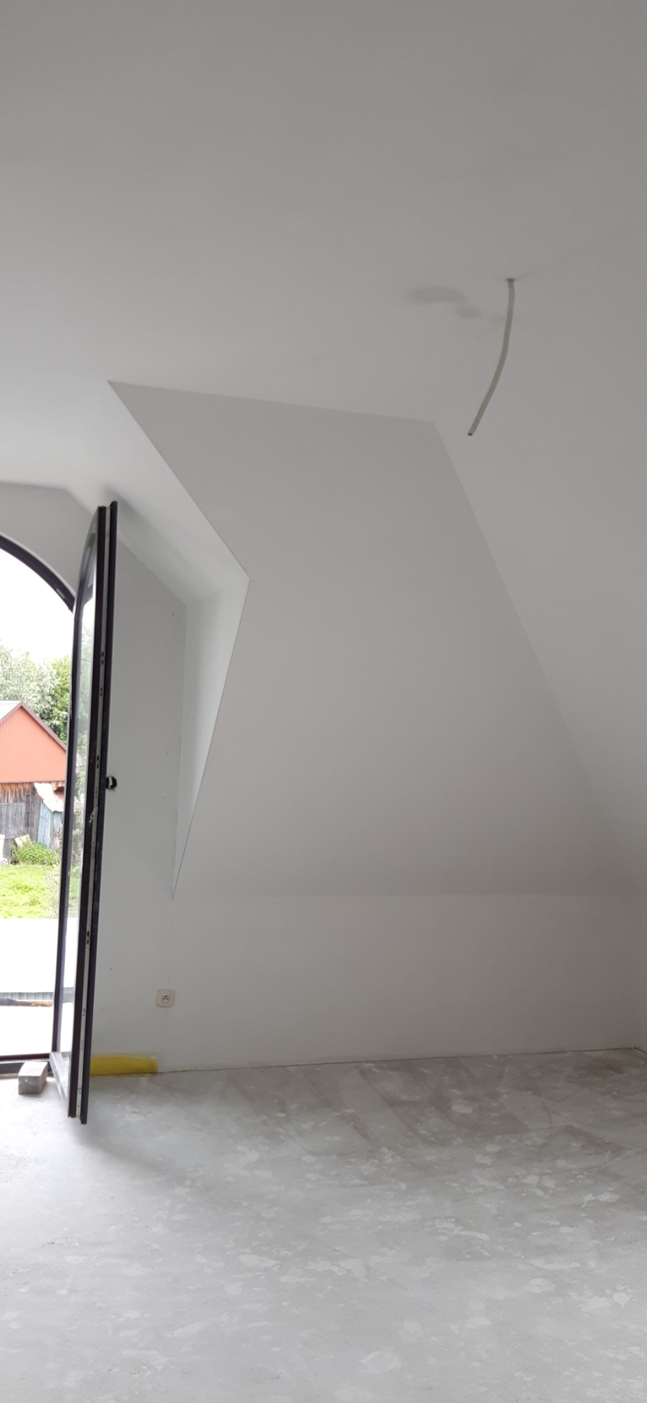 Poddasze z oknem dachowym, świeżo pomalowane na biało, widoczne ślady po malowaniu na podłodze, wystający kabel ze ściany.