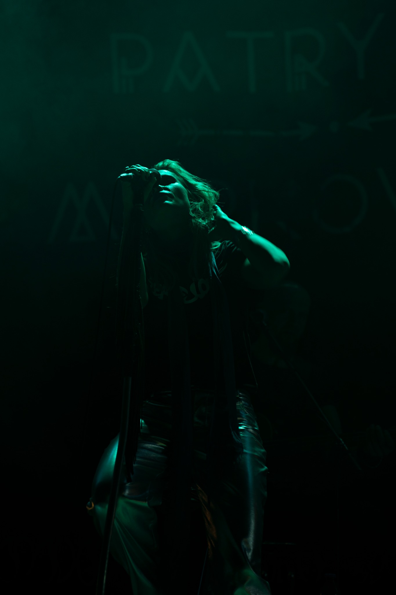 Sylwetka piosenkarki z mikrofonem na scenie, oświetlona zielonym światłem, w tle napis PATRY.