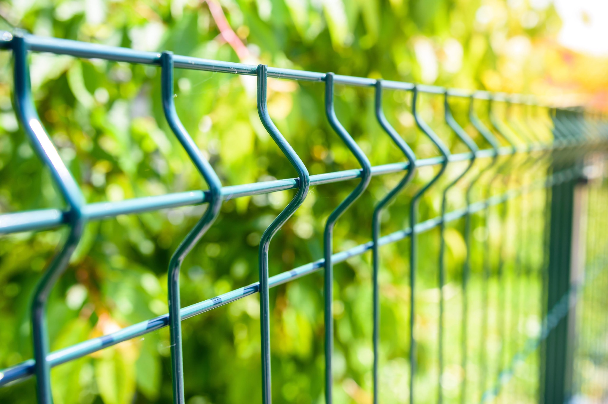 Turkusowy płot panelowy z widocznym zgrzewanym drutem na tle zieleni.